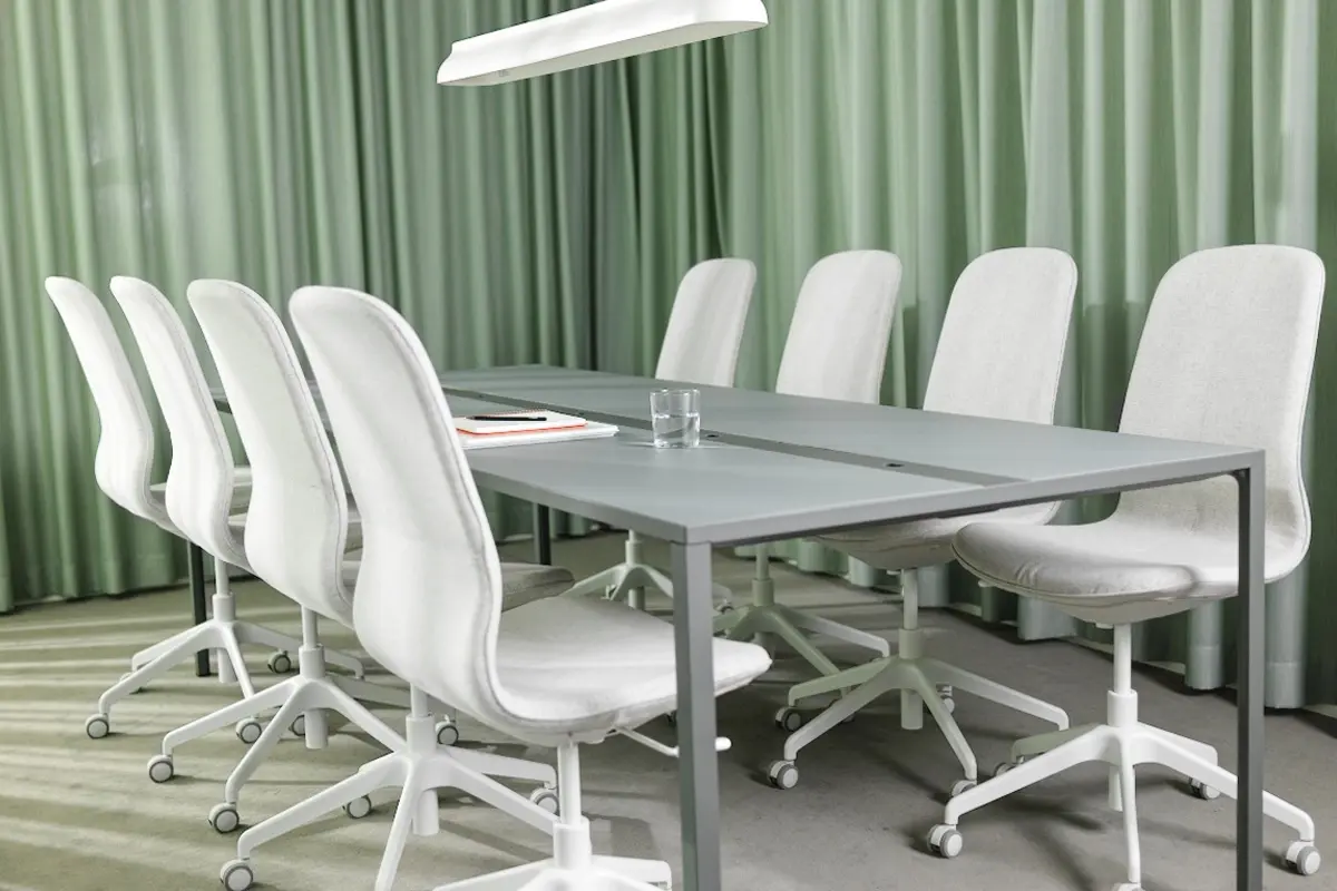 Konferensrum med ett stort bord, 8 stycken vita stolar och en elegant lampa som skapar en professionell atmosfär.