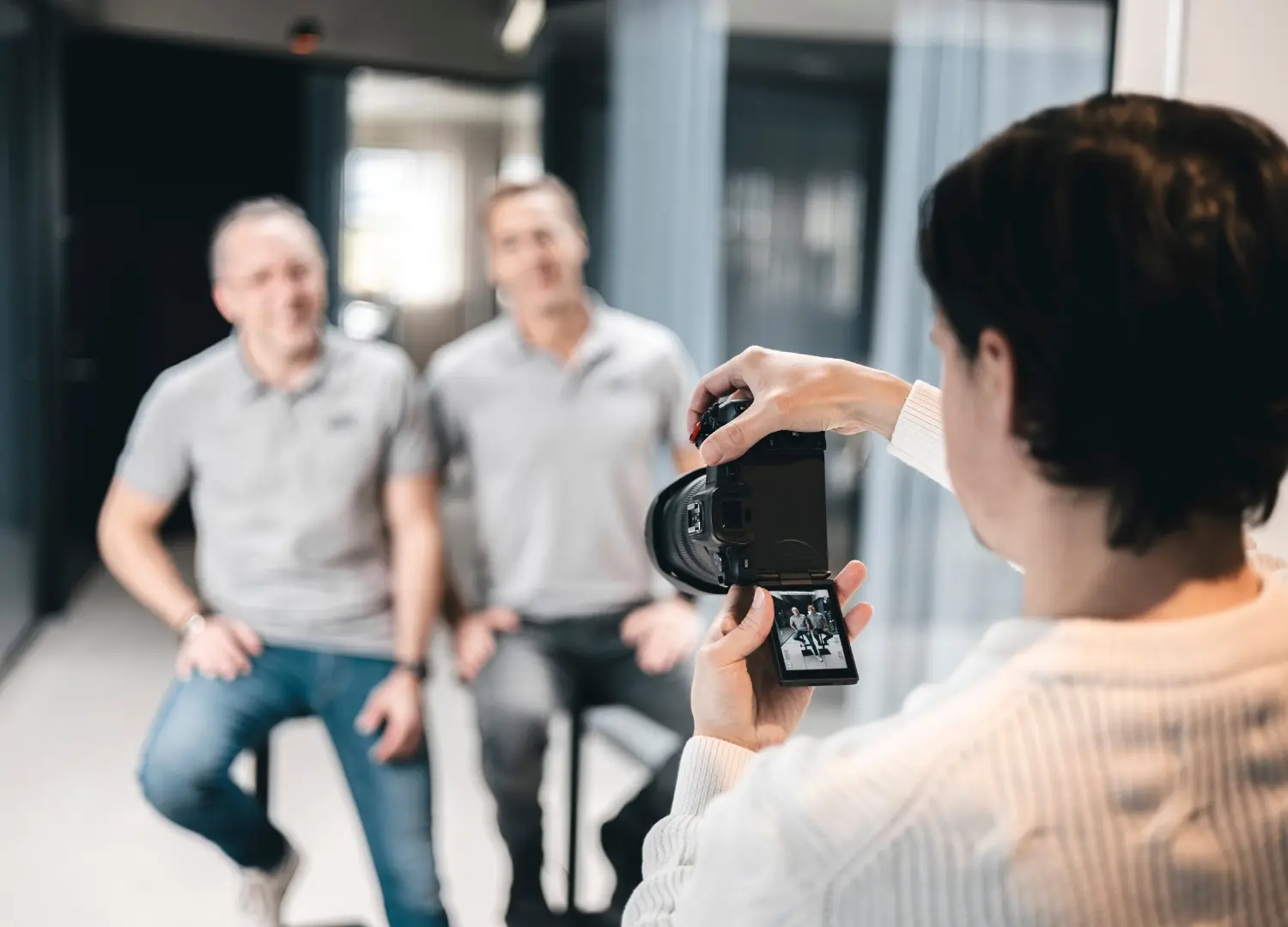 En man fotograferar två andra män i ett rum, fångar deras leenden och stämningen i rummet.